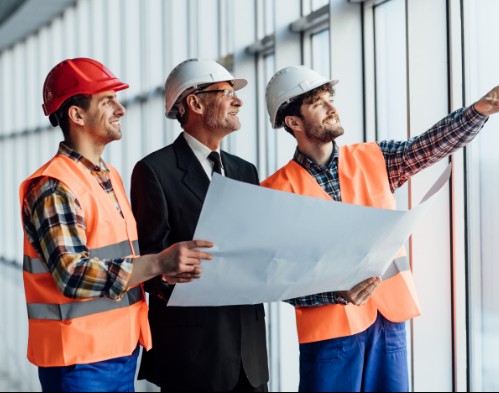 Ingenieros y arquitectos revisando planos en una obra en construcción con ventanales grandes